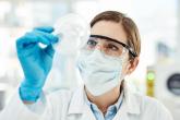 A scientist in protective gear looking at a petri dish