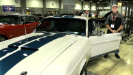 A person standing in the open door of a car at an auto show.
