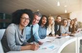 A row of diverse professionals at a long desk all looking at the camera.