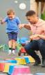 An adult holding a child's hand as they jump along colored spots.