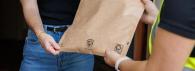 A person handing another a package in a brown Earth Kraft bag.