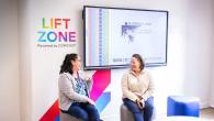 Two people sitting and talking in front of a mural that reads "Lift Zone, Powered by COMCAST"