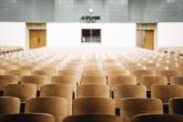 An empty auditorium with rows of wood back seats.