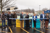 People standing in a parking lot in the rain during a ribbon cutting ceremony