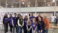A group of people in FedEx Cares t-shirts posing inside a building