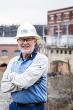 A smiling person with arms crossed in a hard hat. A hydroelectric plant behind them.