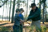 An adult and 2 children hold a tree branch together