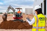 A person looking at a tablet. Another in the distance using a large digging machine.