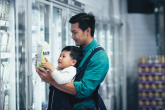 Father with a baby carrier looking at milk label