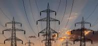 Tall electrical line towers, a setting sun behind them.