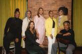 Queen Latifah and a group of others pose in front of a brick wall and yellow curtains