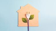 An electric plug with leaves on the cord on top of a cut out house.