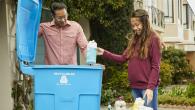 An adult and child putting items into a recycling bin.