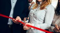 A person cutting a red ribbon with scissors, people on both sides of them.