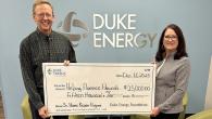 Two people holding a large check. Duke Energy sign on the wall behind them.