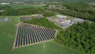 Field of solar panels next to a campus of building in a forested area