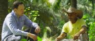 Two people crouched, talking together, in a jungle setting.