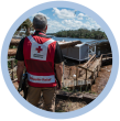 A person in a Red Cross Disaster Relief vest, looking out at damage