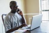 A person in an Army t-shirt on the phone while typing on a laptop