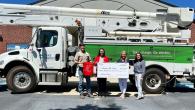 Four people standing in front of a Duke Energy truck, holding a large check