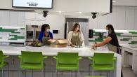 three people in aprons and masks in a large kitchen