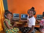 Two smiling children with headphones at a desk with open laptops.