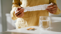 A person reading prescription information with capsules and water on a table in front of them