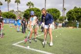 Ashley Sessa demonstrates field hockey stick positioning to a student as other students practice with sticks and balls on the field.