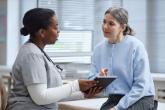 A patient and a health professional are sharing a tablet during a consultation.