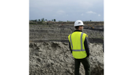 Man in hard hat and yellow vest looking out over mining site