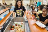 A student pushes a cart to collect food waste from fellow students in a school cafeteria.