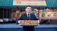 Someone holding up a tray of chicken in front of a restaurant