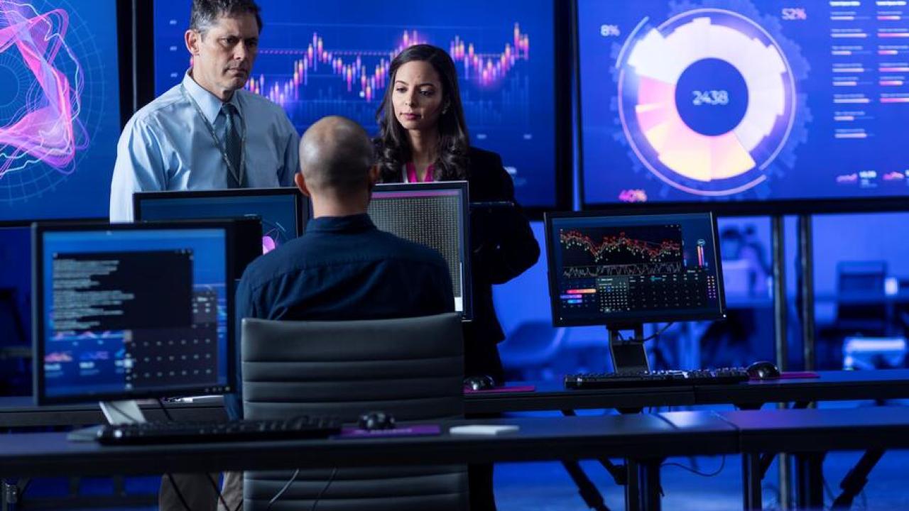 Three people working amongst many computer screens
