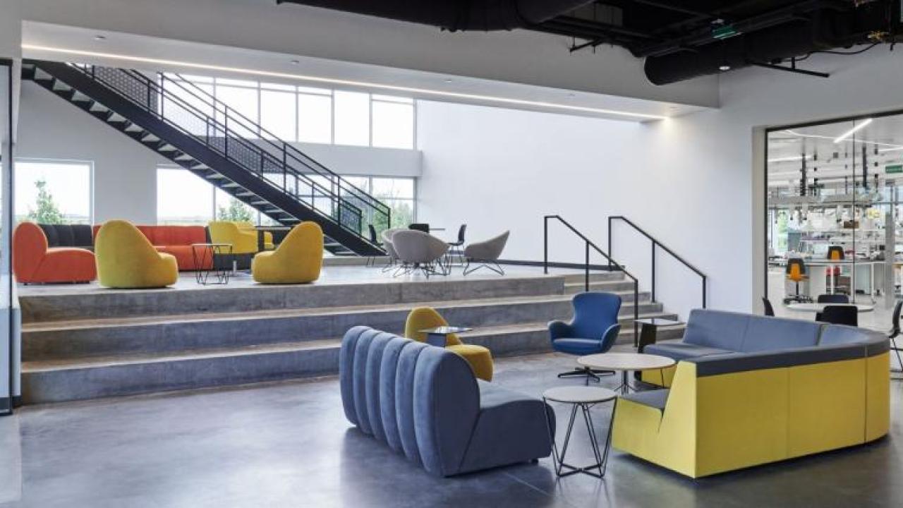 A lobby with blue and yellow seats, which also has a large window looking into a lab