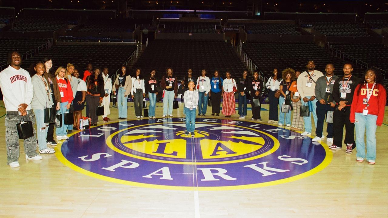 Group of students and professionals standing on the Los Angeles Sparks basketball court for a photo inside Crypto.com Arena.