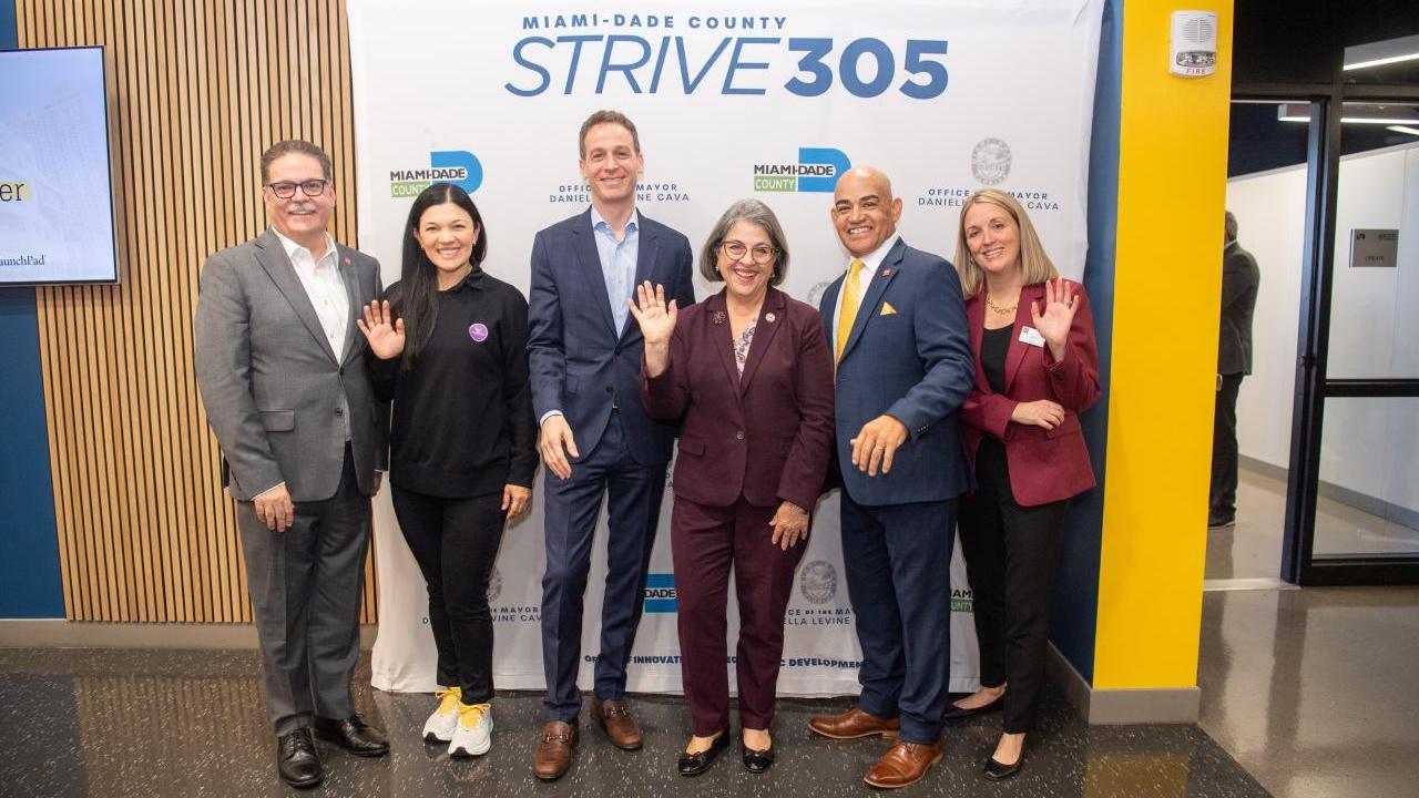 6 men and women standing in front of a sign that says "Strive 305"