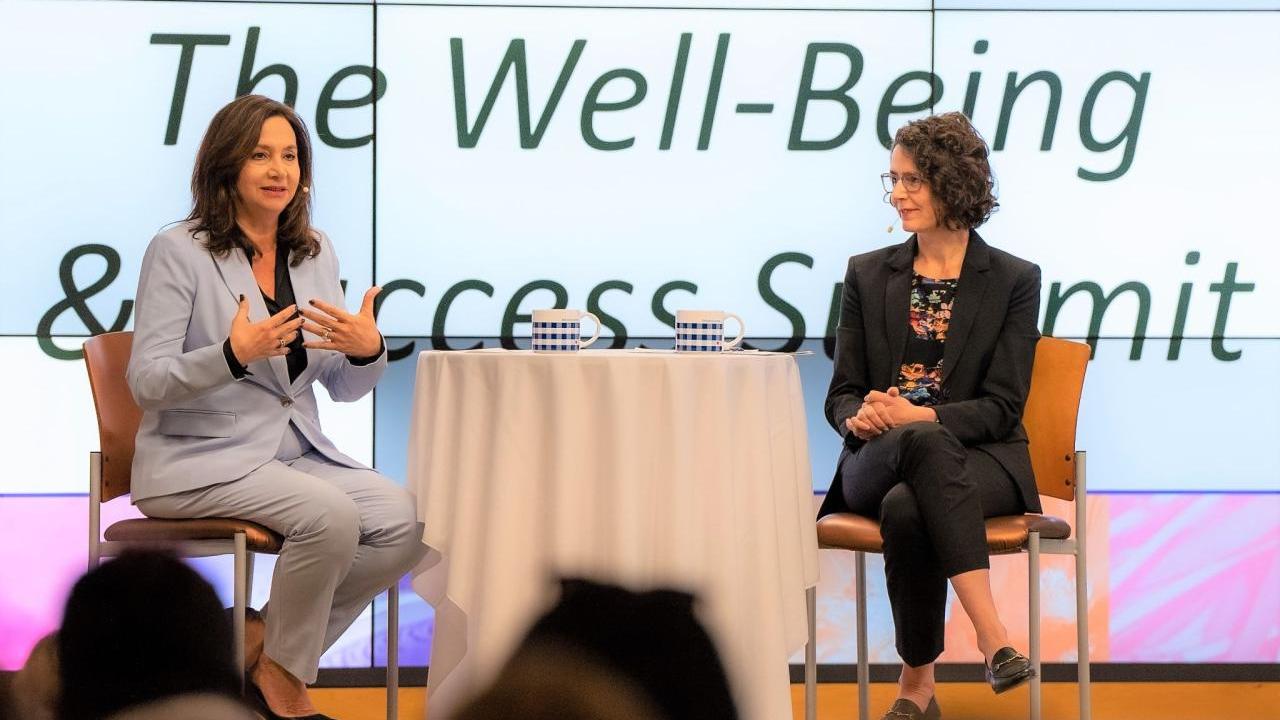 Two people sat on chairs talking on a stage at the Well-Being and Success Summit