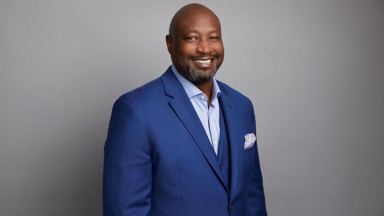 David Casey is wearing a blue suit with a grey background. David is a black man with a shaved head.