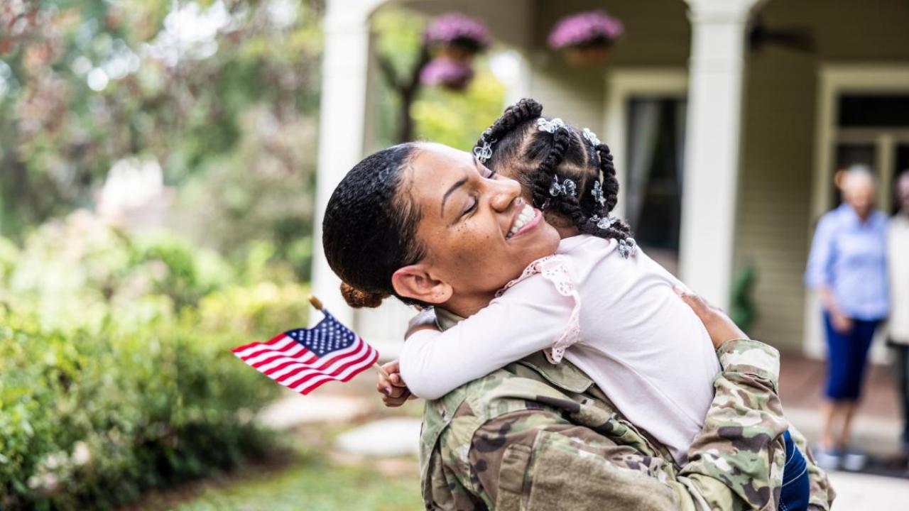 A veteran hugging a young child who is holding a small American flag