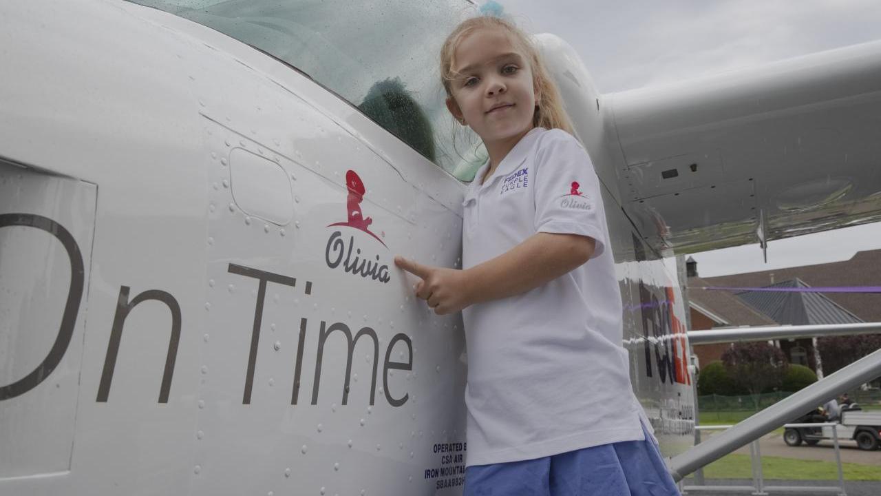 Young girl standing next to plane, pointing at her name (Olivia) printed on it.