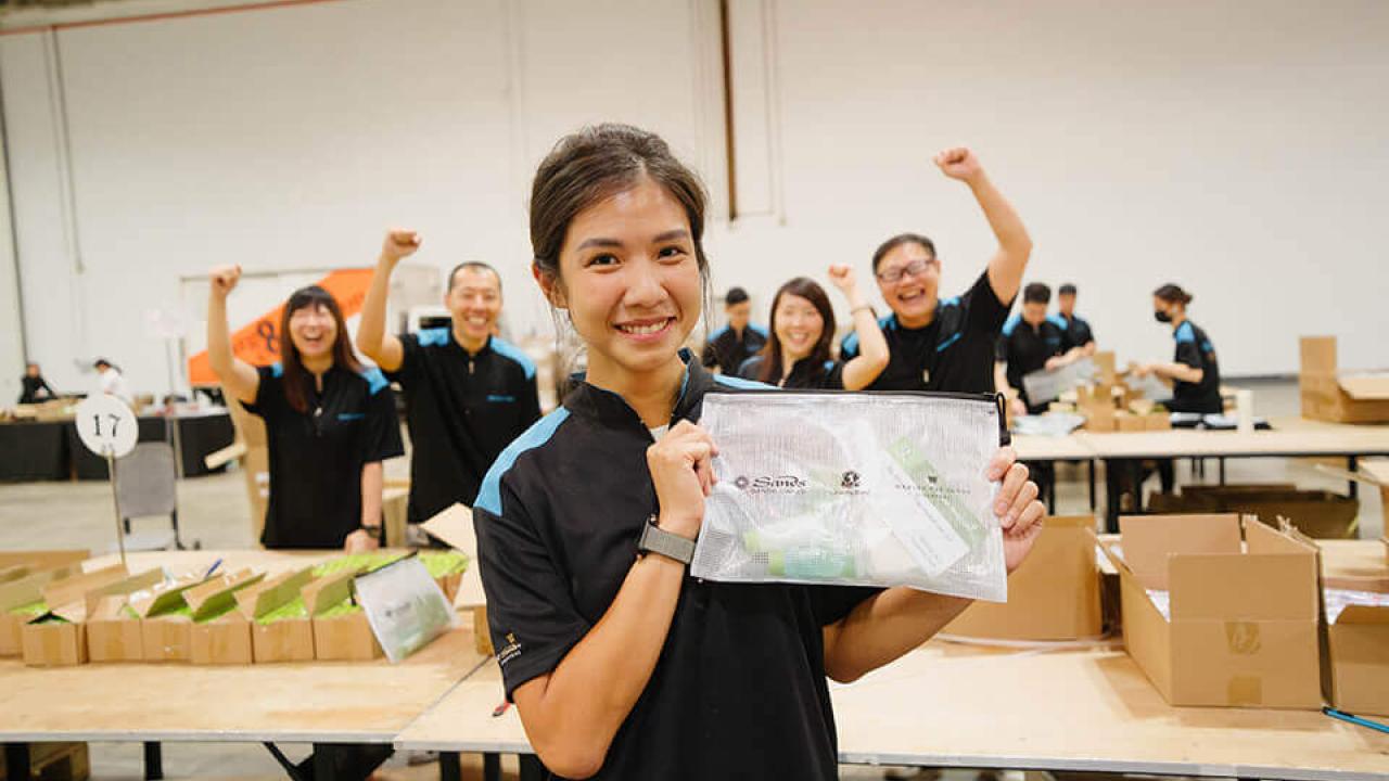 Someone holding up a hygiene kit, with cheering people in the background
