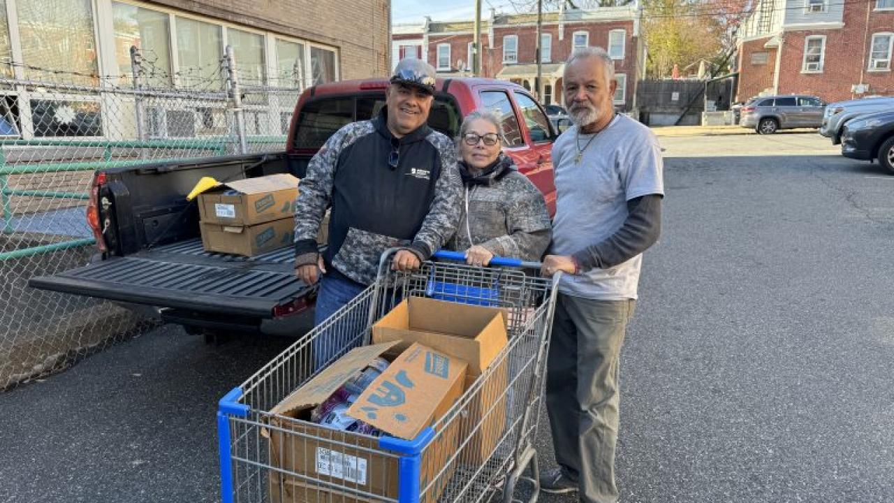 Three people pushing a grocery cart with boxes in it