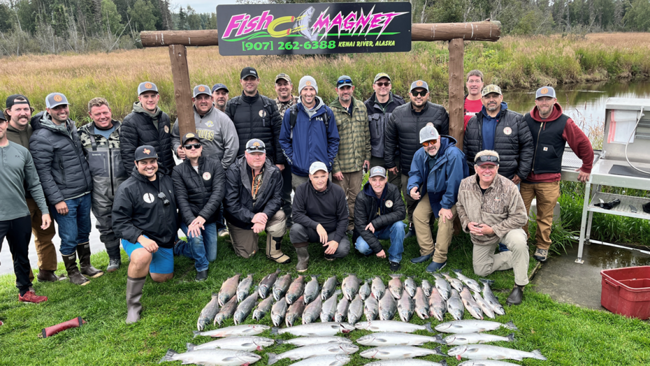 Group posing behind caught fish on the grass