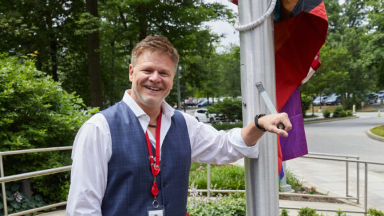 Man standing with hand positioned to raise the Pride Flag at QVC's Studio Park
