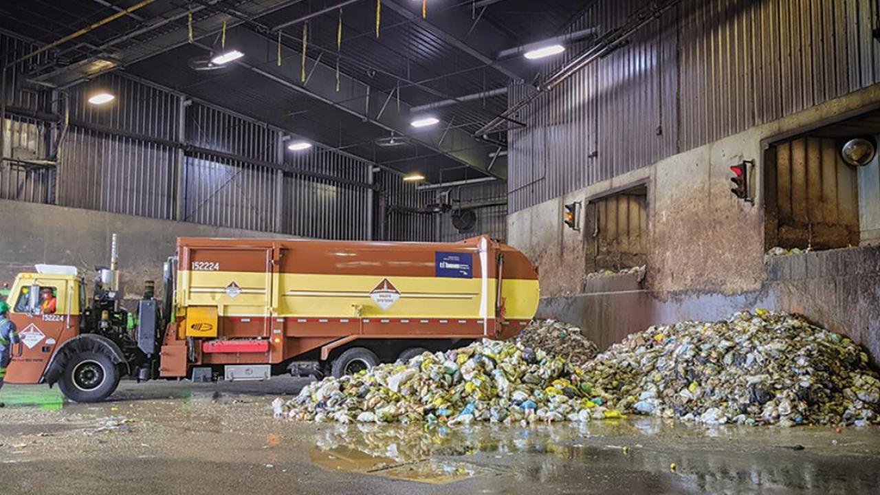 Garbage truck in a bay next to piles of garbage