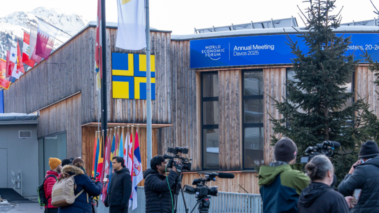 A building with Alps in the background, and people gathering outside