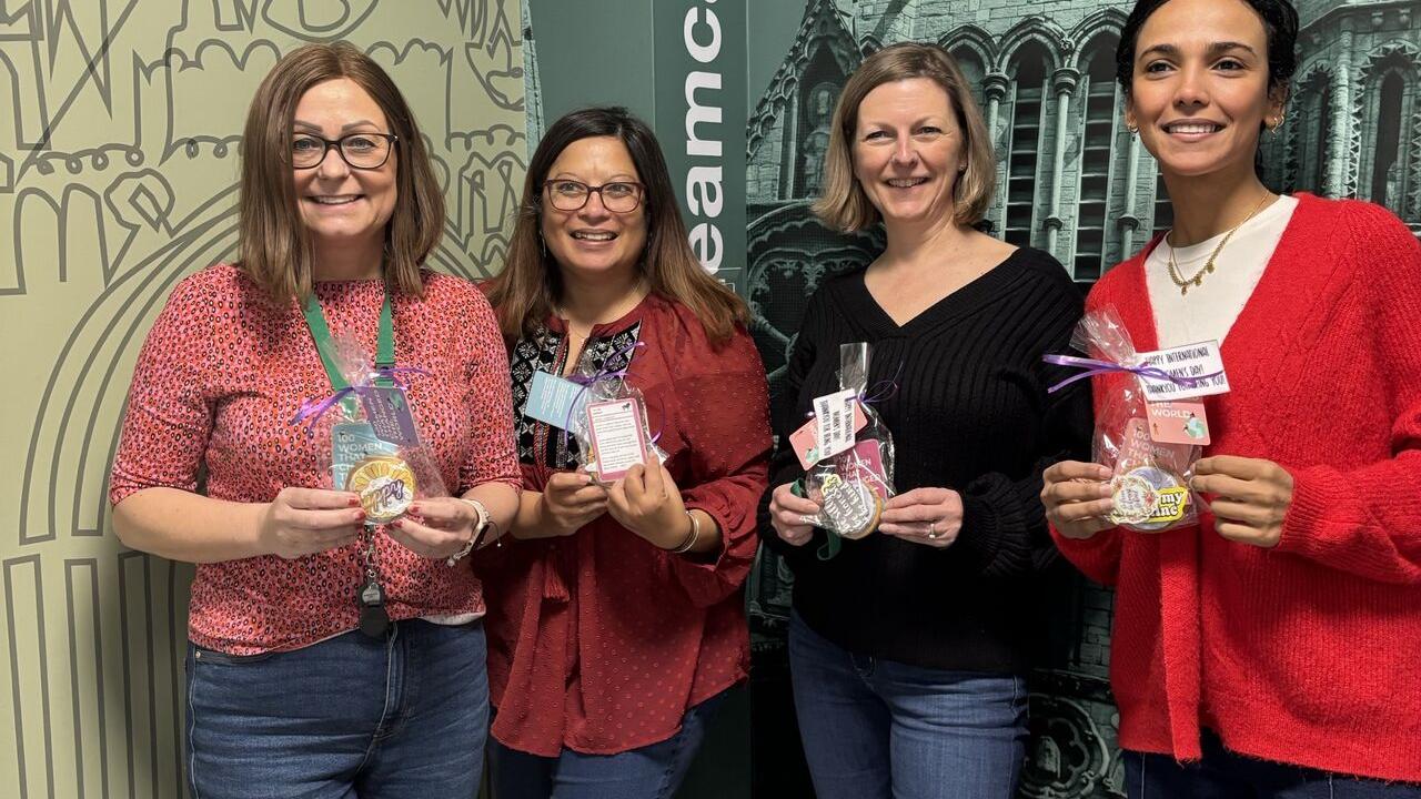 Four women stood next to each other holding a cookie