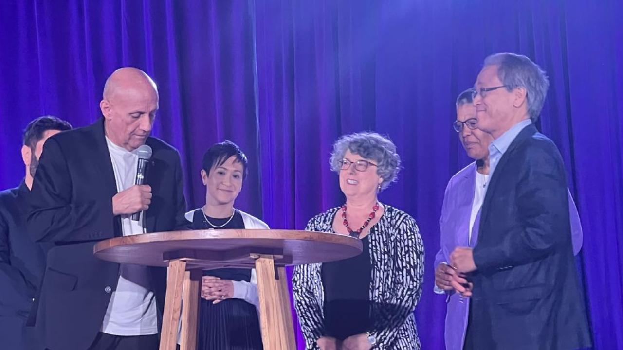 People collected together on a stage around a wooden table