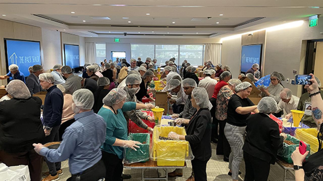 A room full of people in hair nets packing boxes on tables
