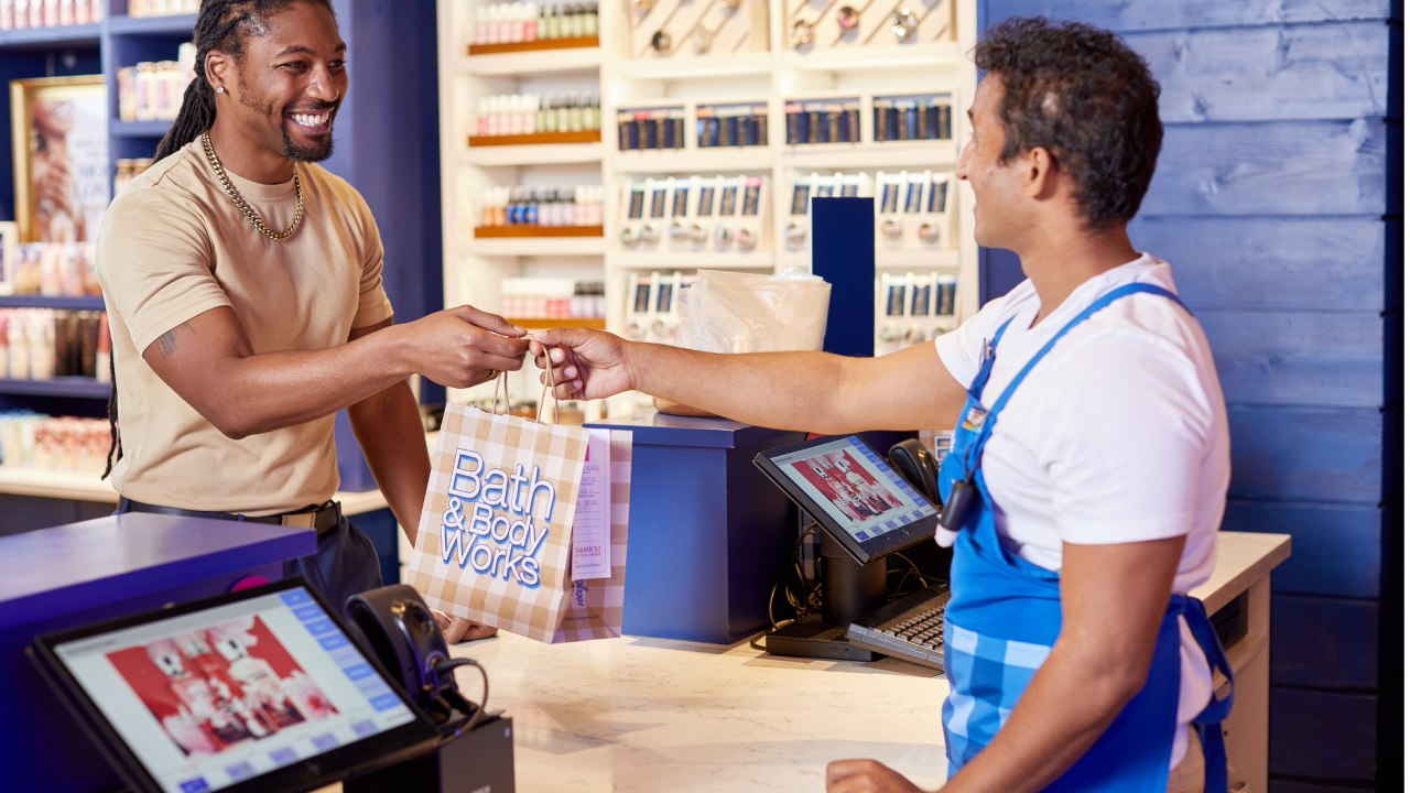 A Bath & Body Works employee handing a bag across the counter to a customer